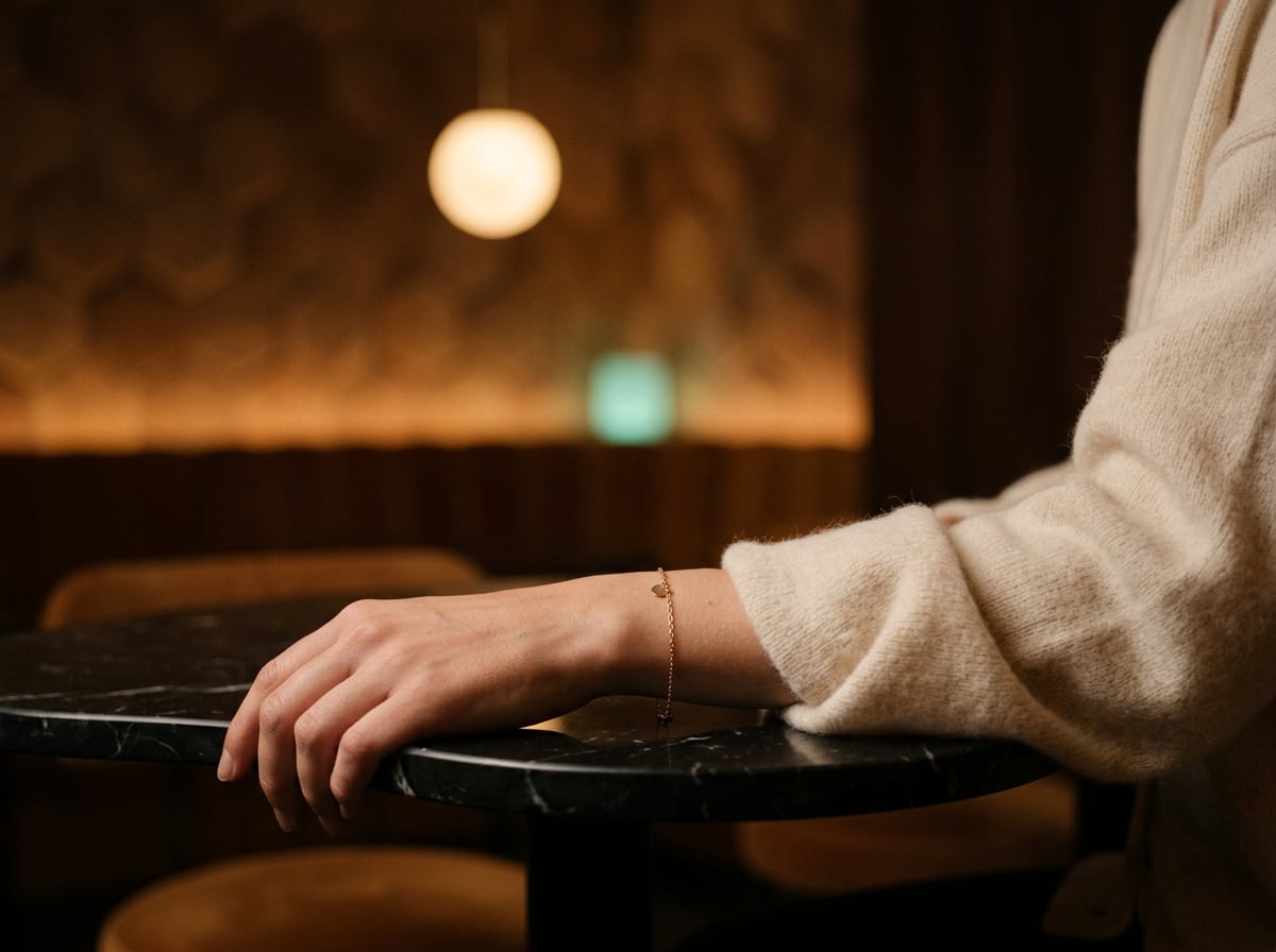 A relaxed wrist in a cream cashmere cardigan resting on a marble table — casual everyday styling